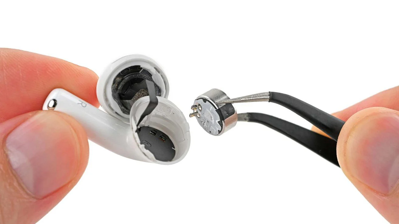 手握住切开的 AirPod 耳塞，而镊子夹住取出的圆形电池